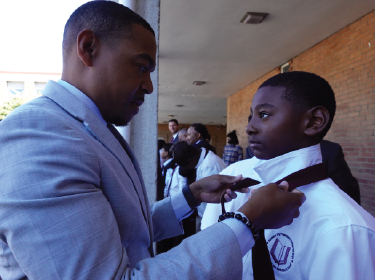 adult tying the neck tie of a young student